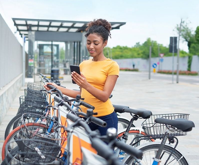 Frau am Handy an einer Bike Sharing Station